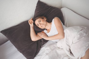 Çekici, gülümseyen, yatakta gerinen genç bir kadın tek başına uyanıyor mutlu bir konsept uyanıyor, sağlıklı bir uykudan sonra rahat bir yatak ve şiltede uyanıyor günaydın.