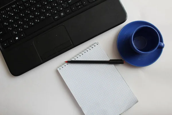 Ofisteki ya da masadaki iş yerinde siyah dizüstü bilgisayarda bir kalem, bir fincan çay ya da kahve var.