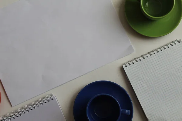 Masanın üzerinde beyaz bir sayfa var yanında bir Kupa yazmak için bir not defteri bir kupa ve bir fincan yeşil ya da mavi ya da metin ya da fotoğraf eklemek için bir yer