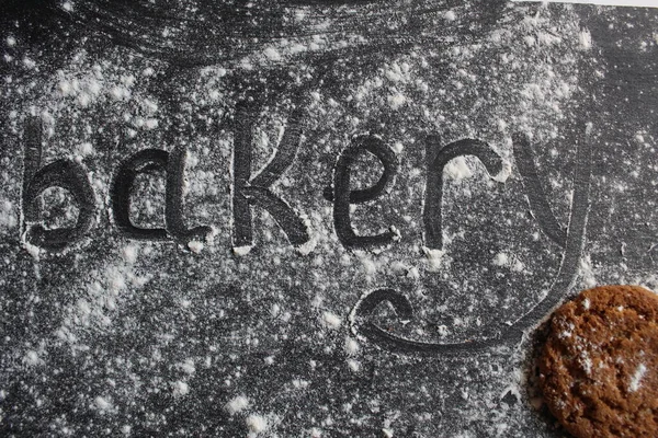 Fırın kelimesi toz şeker ya da un üzerine gri taştan siyah bir zemin üzerine yazılmıştır. Yanında ürünün bir metin ya da fotoğrafı için yeri olan şeker ya da kurabiye parçaları vardır.