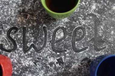 Yazıtlara göre tatlı kelimesi gri taştan siyah arka planda siyah ve beyaz üzerine pudra şekeri ya da un serpiştirilmiş fincanlar var. Fincanlar kırmızı, fincanlar mavi ve çay kahvesi.