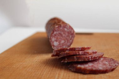 Çiğ sosis tütsülenmiş somun somunu ve ahşap bir kesim tahtasının üzerinde sosis parçaları.