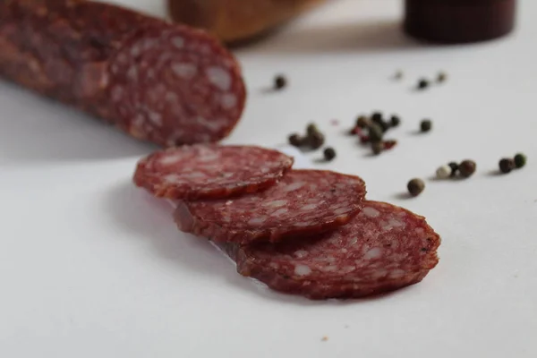 Tütsülenmiş çiğ sosis ve dilimler beyaz bir zemin üzerinde halka şeklinde kesilmiş bezelye ve baget ve arka planda tuzluk.