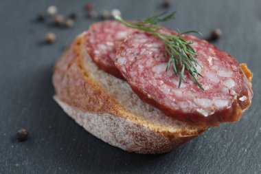 Biberli gri bir taşın üzerinde füme sosisli sandviç.