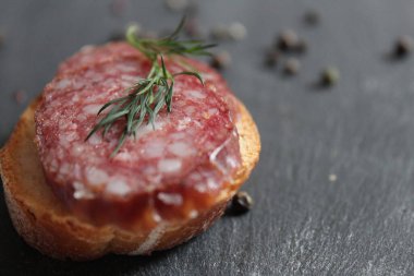 Biberli bezelye ve baharatlı dereotların yanında gri siyah bir taş masanın üzerinde füme sosis ve beyaz ekmekli sandviçlerle dolu bir hayat.