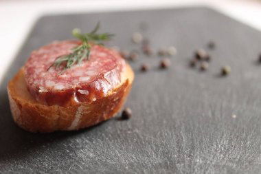 Biberli bezelye ve baharatlı dereotların yanında gri siyah bir taş masanın üzerinde füme sosis ve beyaz ekmekli sandviçlerle dolu bir hayat.