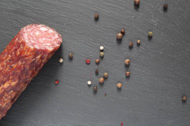 Sol kenarından tütsülenmiş çiğ sosis ve siyah gri bir taşın üzerinde beyaz bezelye kırmızısı.