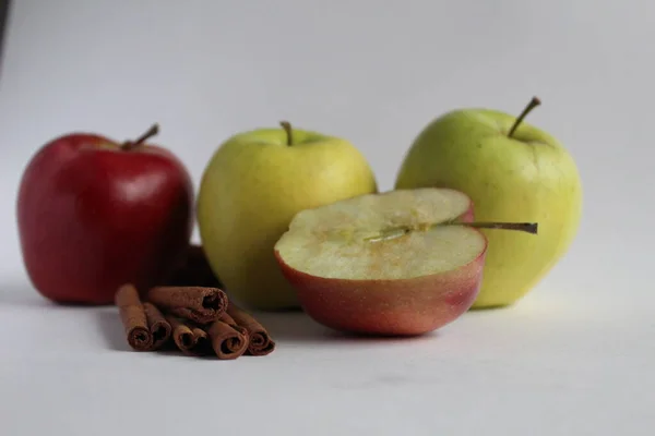 Birkaç elma sarısı yeşil ve kırmızı, beyaz bir zemin üzerinde, tarçın çubuklarıyla yan yana duruyor. Metin eklemek için bir yer var.