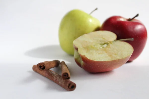 Üç ya da daha fazla tarçın çubuğu ve üç elma kırmızı yeşil sarı ve yarısı beyaz arka planda.