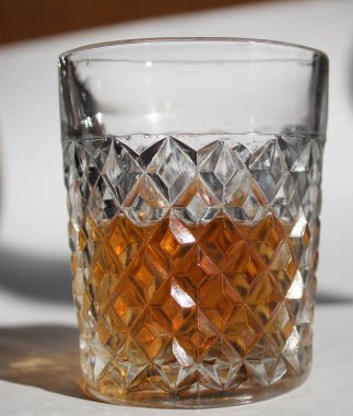 Viski ya da konyaklı cam desenli bir cam beyaz arka planda masanın üzerinde durur. Cam güneş tarafından aydınlatılır.