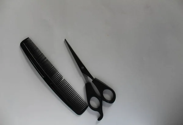 Barber\'s scissors and comb lie together side by side on a white background