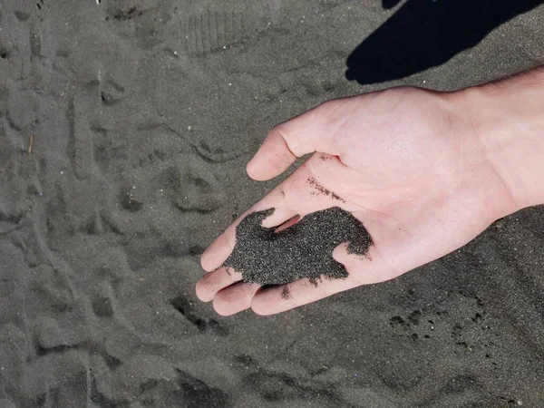 black sand in the hand of a man on the beach Black sand magnetic Ureki Georgia Magnetite