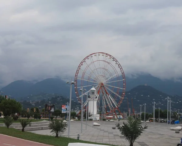 遊園地のカルーセル霧や霞の山を背景に観覧車 Batumi Georgia — ストック写真