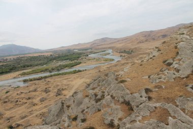 Gürcistan dağlarında gri kahverengi ve bej manzaralı kayalık ve kayalık arazi solda mavi nehir esiyor.