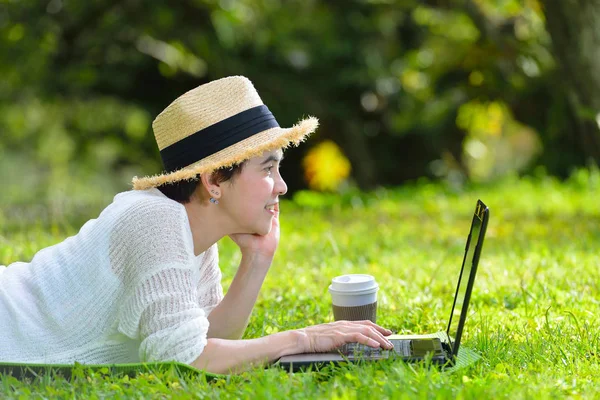 Kvinna liggande på grönt gräs använder bärbar dator — Stockfoto