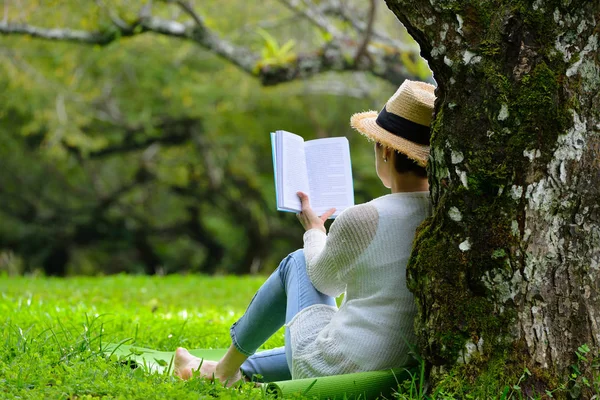 Kobieta siedząca pod drzewem, czytanie książki w parku — Zdjęcie stockowe