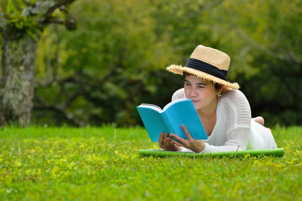 Kvinna liggande på grönt gräs en bok i parken — Stockfoto