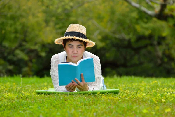 Femme allongée sur l'herbe verte lisant un livre dans le parc — Photo