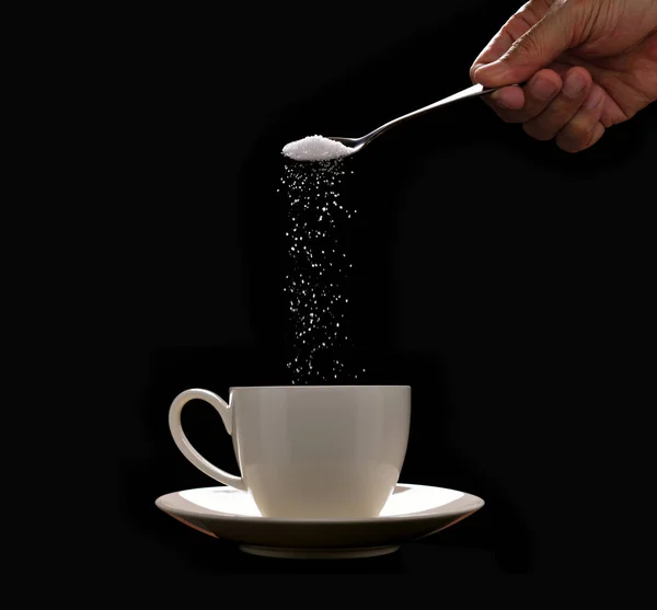 Mettre le sucre à la main dans une tasse de café sur fond noir — Photo