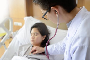Asyalı kadın doktor hasta bir stetoskop ile inceliyor.