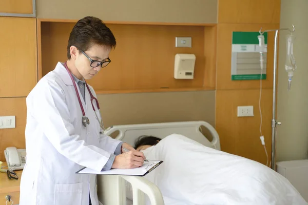 Doctora escribiendo en una historia clínica con paciente acostada en una cama de hospital — Foto de Stock