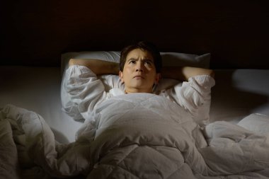 Uykusuzluk çeken bir kadın açık gözlerle yatakta yatıyor.