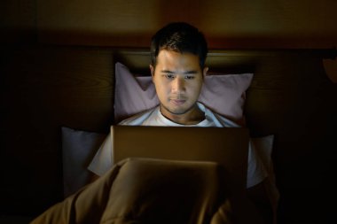 Geceleri yatağında dizüstü bilgisayar kullanan genç adam