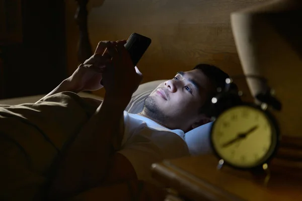 Jeune homme utilisant un smartphone dans son lit la nuit — Photo