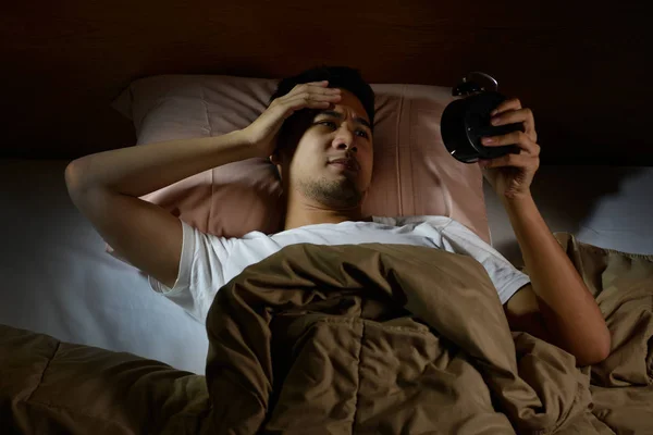 Homem deprimido que sofre de insônia olhando para o despertador deitado na cama — Fotografia de Stock