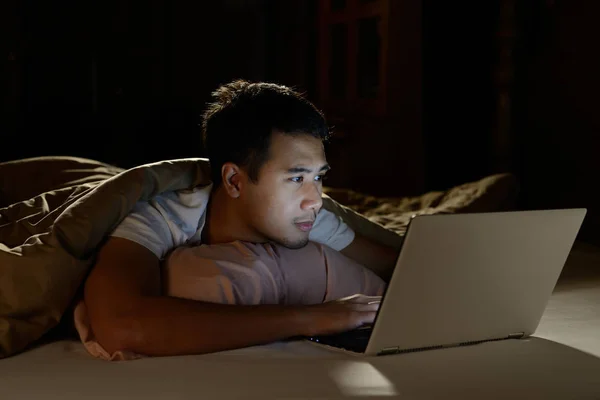 Молодий чоловік використовує ноутбук у ліжку вночі — стокове фото