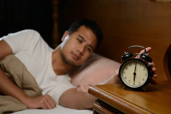 Молодий чоловік вимикає будильник на ліжку — стокове фото