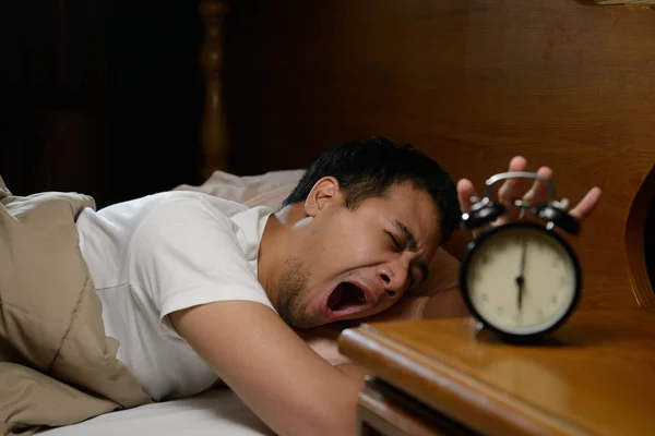 Jeune homme éteignant le réveil sur le lit — Photo