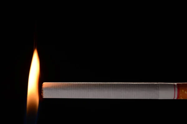 Cigarrillo iluminado por una pequeña llama sobre fondo negro —  Fotos de Stock