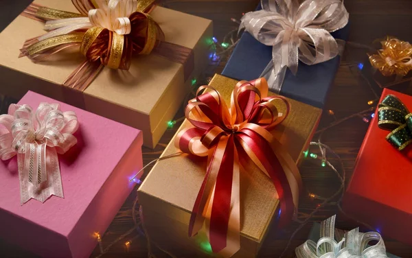 Mezcla de cajas de regalo rematadas con cintas decoradas con iluminación festiva sobre superficie de madera —  Fotos de Stock
