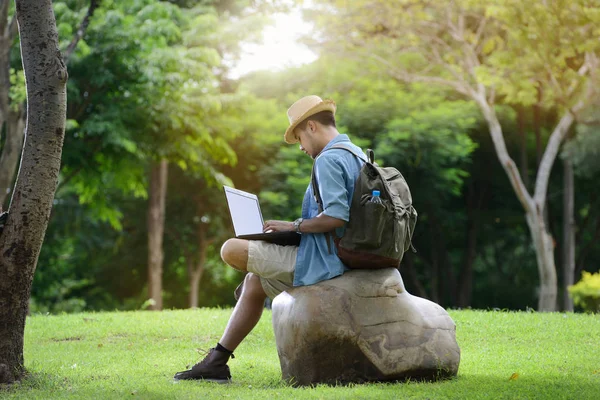 Młody mężczyzna w podróży i pracy na laptopie w parku — Zdjęcie stockowe