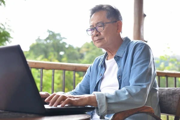 在家庭与绿色花园背景的笔记本电脑工作的老人 — 图库照片