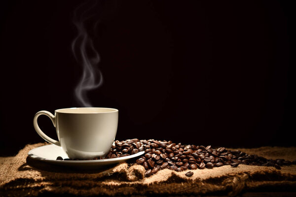 Cup of coffee with smoke and coffee beans on black background