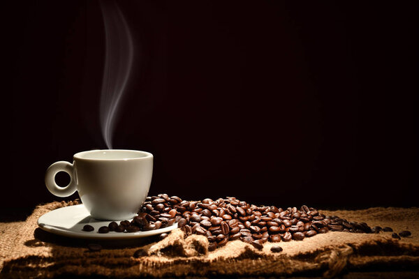 Cup of coffee with smoke and coffee beans on black background