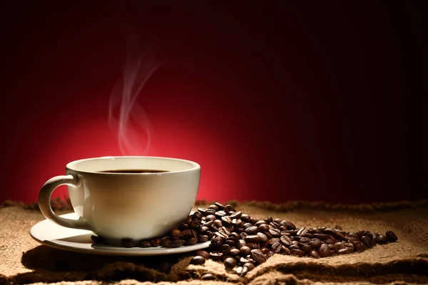 赤みがかった茶色の背景の煙とコーヒー豆とコーヒーのカップ — ストック写真