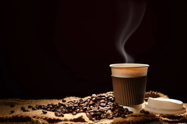 Paper cup of coffee with smoke and coffee beans on black background