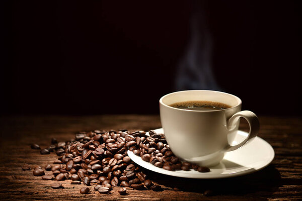 Cup of coffee with smoke and coffee beans on black background