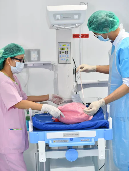 Asian male obstetrician and nurse are examining newborn baby in hospital