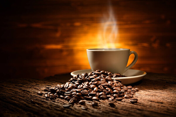 Cup of coffee with smoke and coffee beans on old wooden background