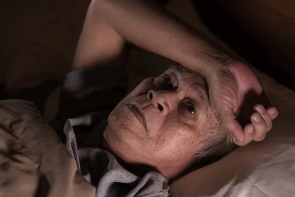 Depressed senior man lying in bed cannot sleep from insomnia