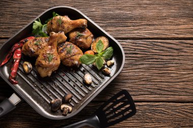 Eski ahşap arka planda tavada çeşitli sebzelerle ızgara tavuk budu.