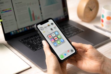 BANGKOK, THAILAND - 14 Nisan 2020: İphone XR 'yi elinde tutan kişi evdeki ekranda sosyal medya simgeleri ile birlikte