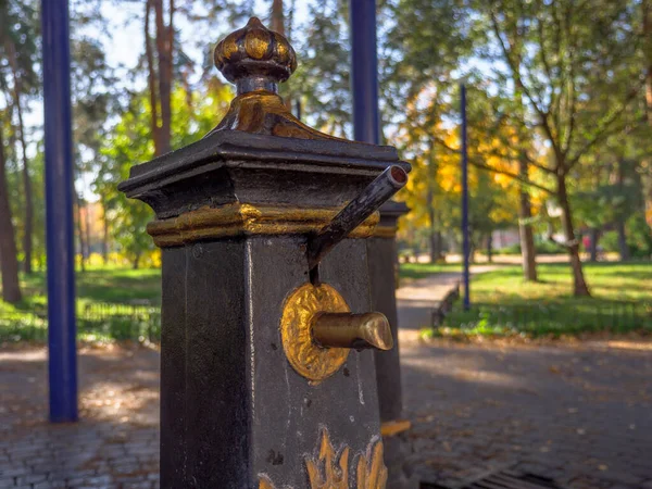 Old-fashioned public metal hand water pumps with golden decoration to draw up clean well water for people to drink and collect it in bottles. Free fresh clean water in a city park.