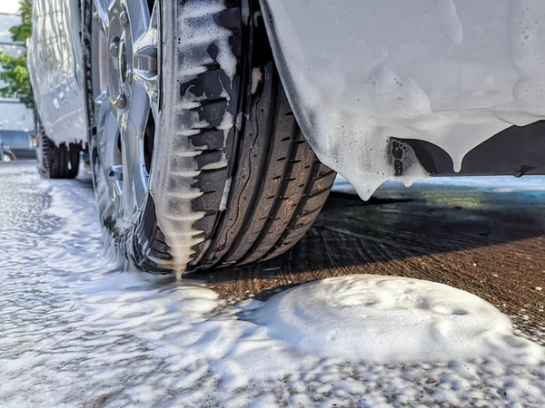 Car wheel and bumper covered with thick fluffy foam dripping on asphalt at a do it yourself car wash. Avoid personal contact and wash alone.
