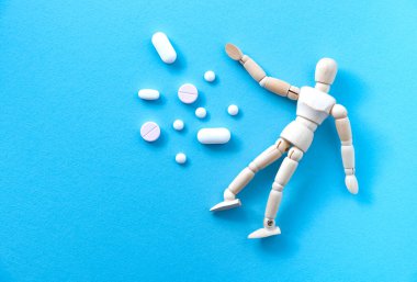 Mavi arka planda minyatür ahşap insan modelinin yanında yığınla hap var. İlaç konseptinin zararlı etkileri