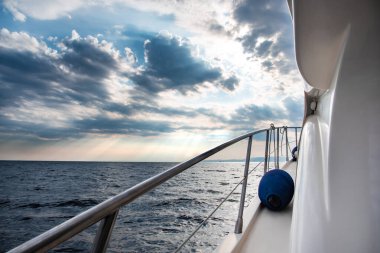 Fırtınalı hava şartlarında gün batımında beyaz lüks yat denize açılıyor. Yattan görünüm